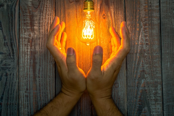 Hand with Glowing bulb on the wood background